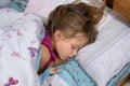 Close up of a face of pretty little child girl with slightly open mouth and scattered around hair sleeping in bed at home