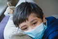 Close up face of Sick child wearing a protective mask, ill child in medical face mask lying head on sofa with sad face,Upset boy Royalty Free Stock Photo