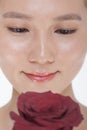 Close-up on the face of smiling beautiful woman looking down at a red rose, studio shot Royalty Free Stock Photo