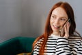 Close up face of smiling young woman talking on mobile phone at home. Cheerful redhead female making answering call by Royalty Free Stock Photo