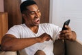 Close-up face of surprised African-American man receiving good news using mobile phone at home. Royalty Free Stock Photo