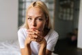 Close up face of thoughtful blonde female sitting alone in living room and serious looking at camera holding hands on Royalty Free Stock Photo