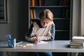 Close-up face of thoughtful schoolboy doing homework writing to notebook with pen looking on book. Royalty Free Stock Photo