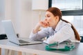 Close-up face of tired exhausted young female doctor wearing white coat yawning during working on laptop. Royalty Free Stock Photo