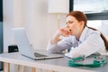 Close-up face of tired exhausted young female doctor wearing white coat yawning during working on laptop. Royalty Free Stock Photo