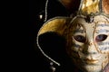 Close up of the face of a young caucasian man with blue eyes wearing a fancy golden Venetian carnival mask on a black background Royalty Free Stock Photo