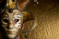 Close up of the face of a young caucasian man with blue eyes wearing a fancy golden Venetian carnival mask on a golden textured Royalty Free Stock Photo