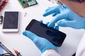 Close up faceless portrait of person`s hand in blue rubber gloves fixing damaged screen of mobile phone, unknown person sitting a