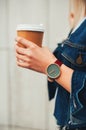 Close up fashion details, young fashionable woman in jeans jacket holding coffee cup. wearing casual unusual watch. Female in