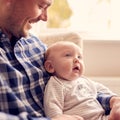 Close Up Of Father Cuddling Baby Son Sitting On Lap In Lounge Chair At Home Together Royalty Free Stock Photo