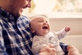 Close Up Of Father Cuddling Laughing Baby Son Sitting On Lap In Lounge Chair At Home Together Royalty Free Stock Photo