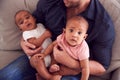 Close Up Of Father Sitting On Sofa At Home Cuddling Baby Son And Daughter