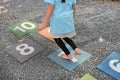 Close-up feet of little girl play jumping on colourful hopscotch playground markings numbers on stone at pavement