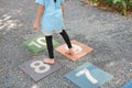 Close-up feet of little girl play jumping on colourful hopscotch playground markings numbers on stone at pavement