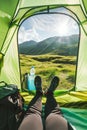 Close up of feet in a tent, a woman lying inside a green popup camping tent with a view of a grassy mountain landscape Royalty Free Stock Photo