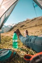 Close up of feet in a tent, a woman lying inside a green popup camping tent with a view of a grassy mountain landscape Royalty Free Stock Photo