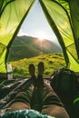 Close up of feet in a tent, a woman lying inside a green popup camping tent with a view of a grassy mountain landscape Royalty Free Stock Photo