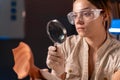 Close-up of a female archaeologist scientist examining an ancient artifact through a magnifying glass while working late