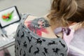 Close-up of a female artist making a color tattoo on the leg of a young girl. Rear view from the back.