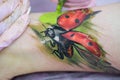 Close-up of a female artist making a color tattoo on the leg of a young girl. Tattoo artist stuffs a ladybug on a