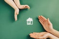 Close up of female and child hands holding white paper house and heart on green background. Family home and real estate concept. Royalty Free Stock Photo