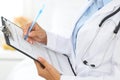 Close-up of a female doctor filling up medical form at clipboard while standing straight in hospital