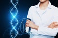 Close up of female doctor with folded arms and glowing DNA helix hologram on background. Medicine and bioengineering concept
