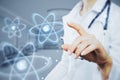 Close up of female doctor hand pointing at abstract glowing atom hologram on blurry hospital or clinic interior background. Royalty Free Stock Photo