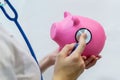 Close-up Of a female Doctor Holding a cute pink piggy Bank and listening to it with a stethoscope on a white background. Women`s h Royalty Free Stock Photo