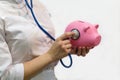 Close-up Of a female Doctor Holding a Stethoscope and listening to a beautiful pink piggy Bank on a white background. Nurse`s hand Royalty Free Stock Photo