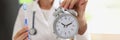 Female doctor stomatologist holding toothbrush and alarm clock in hands