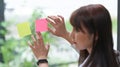 Female employee putting colorful sticky notes on glass wall.