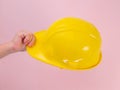 Close-up of female engineer hand holding yellow safety helmet on pink background. Human hand holding a hard hat Royalty Free Stock Photo