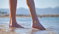 Close up of female feet walking barefoot on white grainy sand of golden beach on blue ocean water background