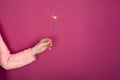 Close up of female hand with burning Christmas sparkler on pink background. Copy space