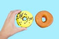 Close-up of a female hand grabs one of two donuts on a blue background. View from above.