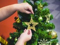 Close-up female hand hanging christmas decorative toys star gold on Christmas tree branch Royalty Free Stock Photo