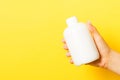 Close up of female hand holding cosmetics bottle at yellow background with copy space Royalty Free Stock Photo