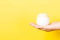 Close up of female hand holding cosmetics jar at yellow background with copy space Royalty Free Stock Photo