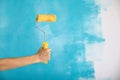 Close up of female hand holding paint yellow roller over blue background-repair, construction and building tools concept. Royalty Free Stock Photo