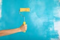 Close up of female hand holding paint yellow roller over blue background-repair, construction and building tools concept. Royalty Free Stock Photo