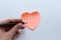 Close-up of female hand holding a pencil above pink heart-shaped sticky note with hand written word `Mum` on it on white backgroun Royalty Free Stock Photo
