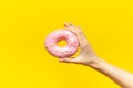 Close-up of female hand, holding pink donut on background of yellow color.