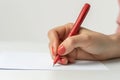 Close-up of a female hand holding a red ballpoint pen, poised to write on a blank sheet of paper, with a focus on the Royalty Free Stock Photo