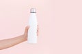 Close-up of female hand holding reusable, steel eco thermo water bottle of white, isolated on background of pastel pink color.