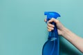 Close-up of female hand holding spray bottle for cleaning with blue pump, on cyan background. Royalty Free Stock Photo