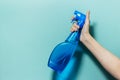 Close-up of female hand holding spray bottle for cleaning with blue pump, on cyan background. Royalty Free Stock Photo