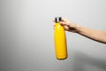 Close-up of female hand holding stainless reusable thermo water bottle of yellow color on grey background Royalty Free Stock Photo