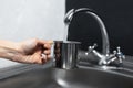 Close-up of female hand holding steel mug under the water tap in kitchen. Background of black and white walls. Royalty Free Stock Photo