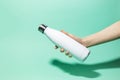 Close-up of female hand holding white reusable steel stainless thermo water bottle isolated on background of aqua menthe color.